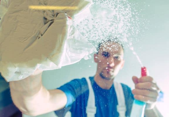 Cleaning Service Worker Men Cleaning Office Windows. Windows Detergent Spraying and Cleaning by Caucasian Male. Cleaning Service Worker.